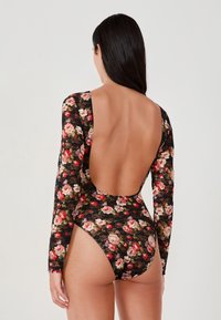 Mouwloos zwemoutfit in zwarte bloemenkant, met een diepe uitsnede aan de achterkant en kleurrijke rozenpatronen. Figuurcorrecte pasvorm met een hoge beenuitsnede.
