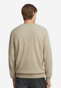 Beige tröja med rund hals, mjuk textur och ribbad mudd och nederkant. Har en enkel design, visad från baksidan.