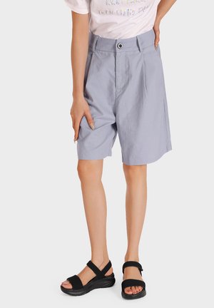 Pantaloni shorts grigi chiari con una vestibilità comoda, dotati di chiusura con bottone e tasche laterali, abbinati a sandali neri con cinturini regolabili.
