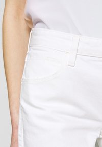 Jeans in denim bianco con un design classico, dotati di tasche laterali, passanti per cintura e cuciture a contrasto. Texture liscia e vestibilità aderente.