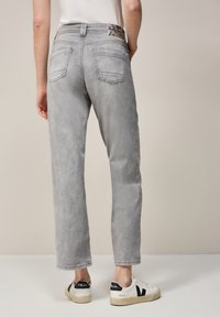 Grijze high-waisted jeans met een ontspannen pasvorm, voorzien van achterzakken en een gedessineerde tailleband. Gepaard met witte sneakers.