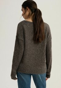 Brązowy sweter dzianinowy wykonany z miękkiego materiału, charakteryzujący się luźnym krojem, prążkowanym dołem i długimi rękawami. W połączeniu z niebieskimi dżinsami.