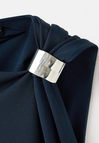 Drappeggio in tessuto blu navy fissato con una fibbia metallica argentata, che mette in mostra una texture liscia e dettagli plissettati. Design semplice ed elegante.