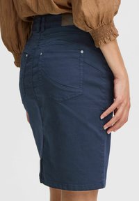 Mörkblå denimkjol med en åtsittande silhuett, med bakfickor, subtila sömnadsdetaljer och en midilängd.