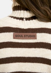 Brown and cream striped knit sweater with a turtleneck. Features a leather tag with "SOUL STUDIO" on the back. Soft texture, ribbed knit.
