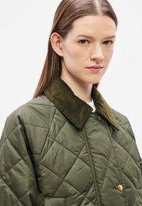 Zöld steppelt dzseki kordbársony gallérral, átlós varrásokkal, arany patentgombokkal és első zsebekkel.