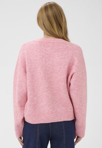Pull en tricot rose avec une coupe décontractée, ourlet côtelé et surface texturée. Modèle présenté de dos sur un fond neutre.