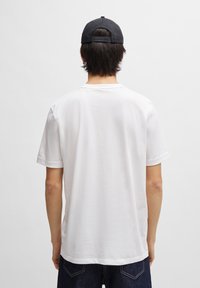 Camiseta de algodón blanca con un corte relajado, presenta mangas cortas y un cuello redondo, vista desde la espalda sobre un fondo básico.