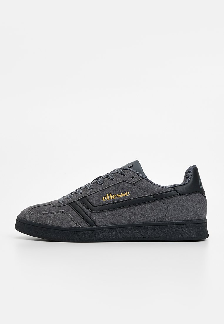 Zapatillas grises con un upper de tejido texturizado y acentos de cuero liso. Cuenta con una suela de goma negra y la marca "ellesse" en dorado en el lateral.