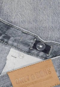 Tissu en denim gris avec un bouton noir, un fermoir à pression argenté et une étiquette en cuir beige embossée avec "ONLY & SONS".