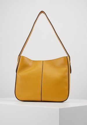 Gelbe Leder-Schultertasche mit einem einzelnen Riemen, schwarzer Umrandung und einer vertikalen Naht in der Mitte, präsentiert auf einem weißen Podest.