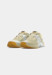 Ζευγάρι αθλητικών παπουτσιών σε μπεζ και άσπρο, με πορτοκαλί σόλες, μαύρο λογότυπο swoosh και λευκή ετικέτα στις κορδόνες, σε λευκό φόντο.