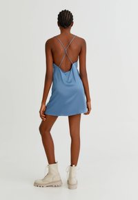 Blå satin klänning med tunna korsade band på baksidan. Modellen matchar den med krämfärgade snörade ankelstövlar.