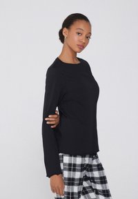 Černý dlouhý rukáv s kulatým výstřihem, který má volný střih a texturovanou látku. Spárováno s černobílými kostkovanými kalhotami.