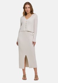 Rippstrick-Zweiteiler in Hellbeige, bestehend aus einer kurz geschnittenen Strickjacke mit V-Ausschnitt und Knopfverschluss sowie einem langen Rock mit einem Schlitz auf der Vorderseite.