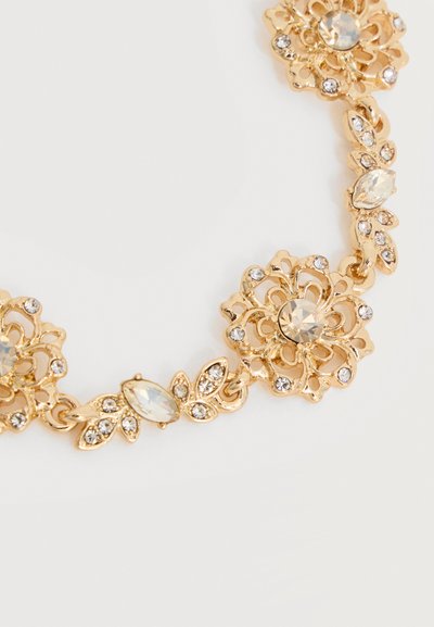 Κολιέ με χρυσή απόχρωση και λουλουδένιο σχέδιο, διακοσμημένο με διαυγή κρύσταλλα και περίτεχνα φιλιγκράν, σε λευκό φόντο.