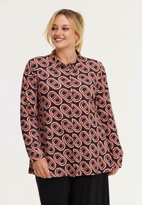 Schwarze Hemdbluse mit ovalem Muster in Rot und Weiß. Lange Ärmel, Kragen und goldene Knöpfe unterstreichen das Design.