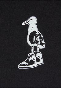 Tela negra con un gráfico blanco de un pájaro de pie sobre una zapatilla, mostrando el contorno del pájaro y los detalles de la zapatilla.