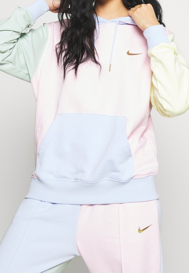 Mikina v pastelových barvách se zlatým logem Nike, obsahující klokaní kapsu, kapuci na šňůrku a design s barevnými bloky v jemných odstínech růžové, modré a zelené.