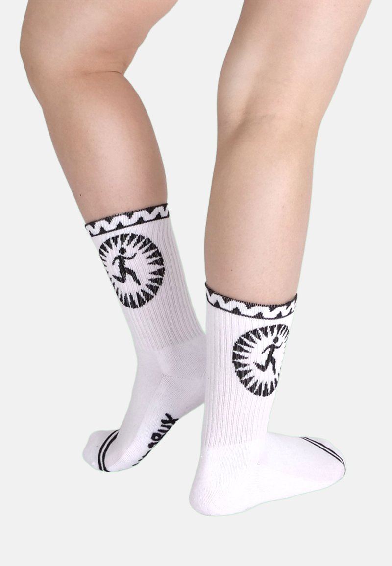 Weiße Baumwollsocken mit schwarzem Zickzackrand, versehen mit einem runden Grafikdesign und einer Personensilhouette. Strukturierte Rippenstrickmuster und kontrastierende Streifen an den Zehen.