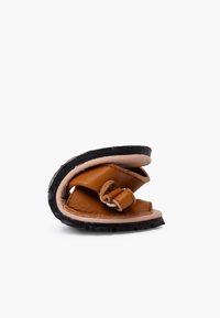 Sandalo in pelle marrone piegato con suola in gomma nera. Presenta una forma curvata e una cintura regolabile con una fibbia in metallo.