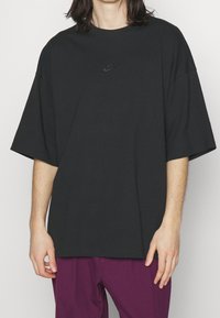 Černé oversized tričko vyrobené z bavlny s malým černým logem Nike na hrudi. Tričko má kulatý výstřih a krátké rukávy.