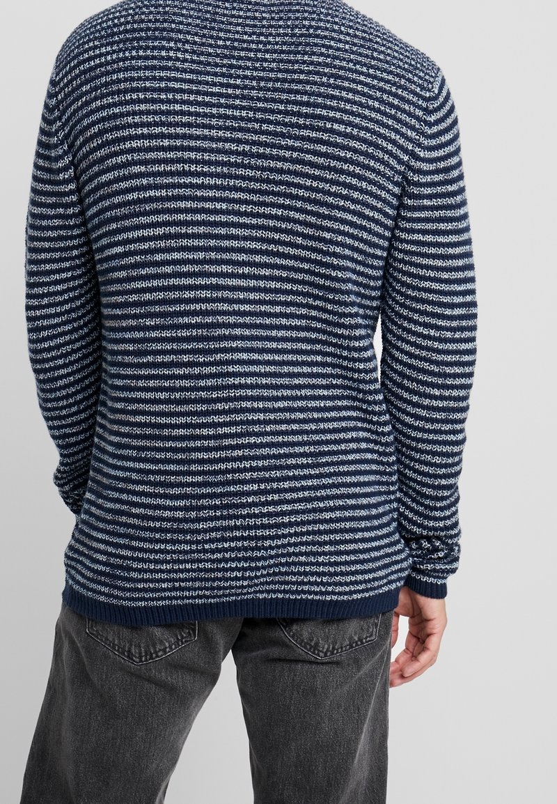 Maglione a righe blu navy con strisce bianche di larghezze variabili, polsini e orlo a costine, texture morbida, design morbido e rilassato.