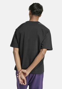 Schwarzes Baumwoll-T-Shirt mit kurzen Ärmeln und Rundhalsausschnitt. Verfügt über ein schlichtes Design mit lockerer Passform und einer flachen Nahtdetails auf der Rückseite.