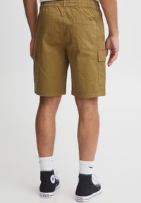 Khaki cargo shorts with an elastic waistband, side pockets, and a back pocket. Textured cotton fabric. Worn with black high-top sneakers.