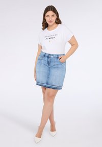 Camiseta blanca con texto negro y un gráfico de sol, combinada con una falda de mezclilla azul clara que tiene bolsillos y un detalle de dobladillo deshilachado.