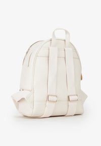 Zaino in pelle bianca con forma arrotondata, due spallacci in tessuto e dettagli in metallo dorato. Superficie testurizzata e chiusura con zip.