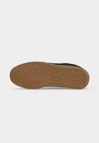 Semelle de chaussure avec une bande de roulement en caoutchouc marron et à motifs présentant des rainures circulaires et des bords texturés sur une semelle noire.