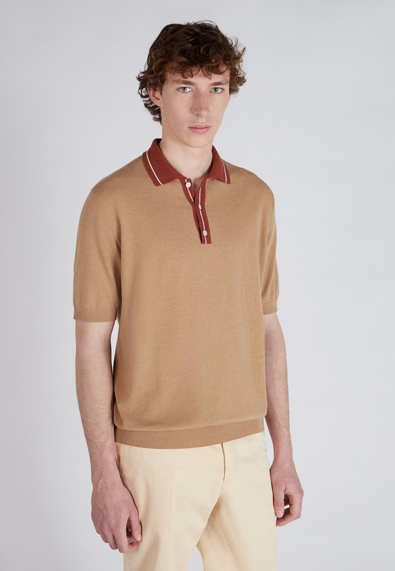 Polo shirt en maille beige à manches courtes, avec un col marron contrastant et une fermeture à boutons, ainsi qu'un ourlet et des poignets côtelés.