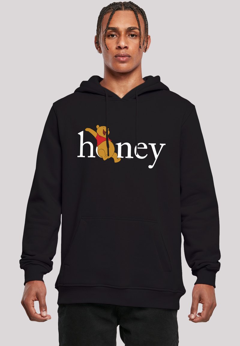 Svart hettegenser med stor hvit "honey" tekst og en tegneserie-bjørn i rød skjorte, designet med kengurulomme og avslappet passform.