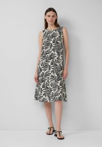 Robe noire et blanche à motifs de feuilles, avec une jupe évasée, sans manches et en tissu léger, accompagnée de sandales plates simples.