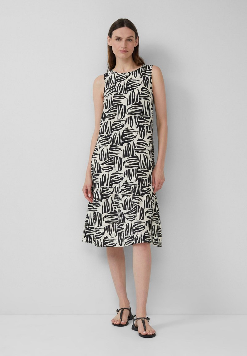 Robe noire et blanche à motifs de feuilles, avec une jupe évasée, sans manches et en tissu léger, accompagnée de sandales plates simples.