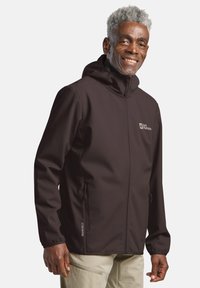Veste softshell marron avec capuche, en matériau léger, deux poches zippées et logo sur la poitrine. Texture lisse, design ajusté.