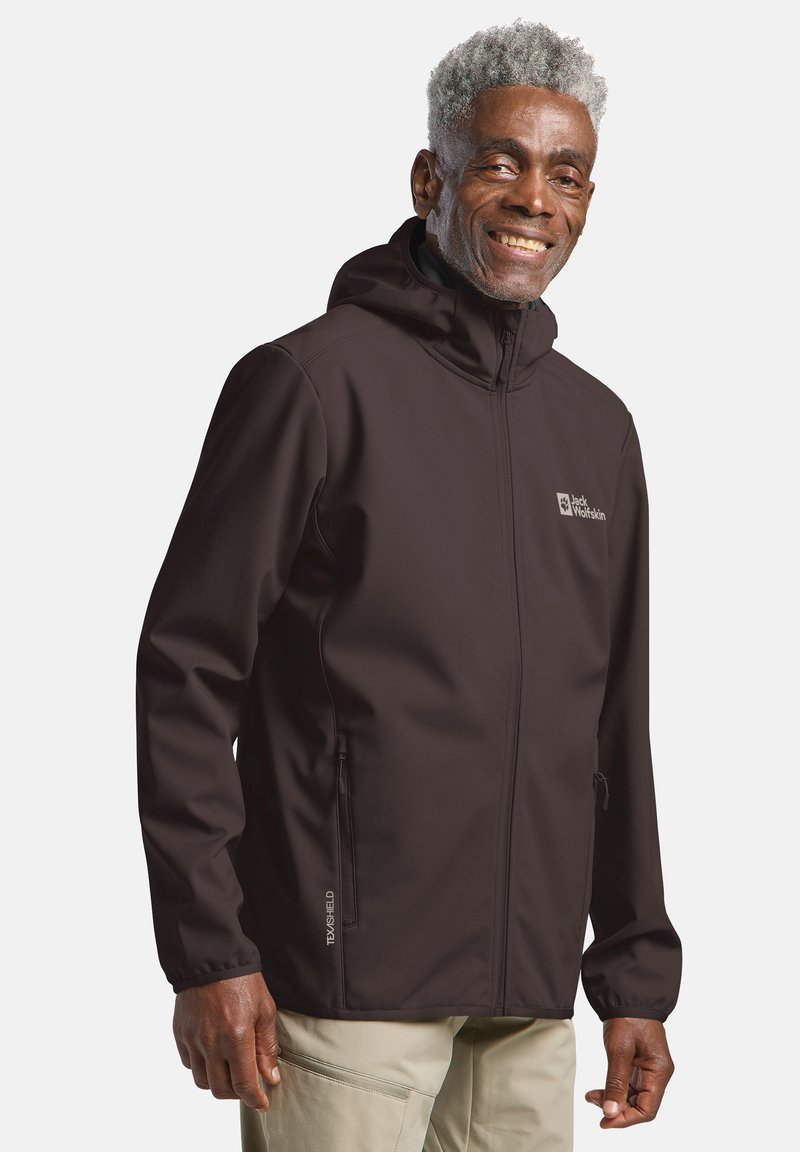 Veste softshell marron avec capuche, en matériau léger, deux poches zippées et logo sur la poitrine. Texture lisse, design ajusté.