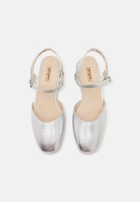 Zapatos slingback metálicos plateados con punta redonda, tacón plano y correa en el tobillo. Textura suave con diseño minimalista.