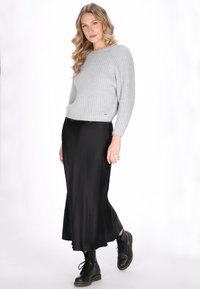 Lichtgrijze gebreide trui met ribbeltextuur, gecombineerd met een zwarte satijnen maxirok en zwarte veterschoenen.