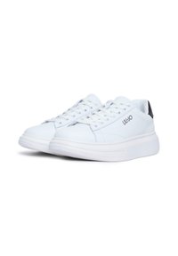 Sneaker vegan in pelle bianca con una texture liscia, punta rotonda e accento sul tallone nero a contrasto. Presentano lacci e un sottile logo del marchio.
