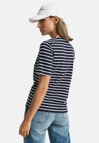 Marineblå og hvide stribede t-shirt med rund hals og korte ærmer, parret med lyseblå denim jeans; model iført en hvid kasket.