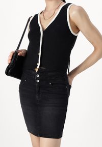 Černý žebrovaný úpletový crop top s bílým lemováním a knoflíky, který je spárován s přiléhavou černou džínovou sukní s vysokým pasem a předními kapsami.