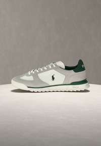 Baskets basses blanches et grises avec des accents verts, lacets blancs, semelle texturée, et logo Polo sur le côté et l'onglet du talon.