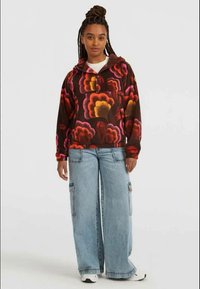 Kapišonas marškiniai rudoje spalvoje su didelėmis gėlių raštais raudona, rožine ir geltona spalvomis. Poruojama su šviesiai mėlynomis plačiaklėmis krovininėmis džinsomis.