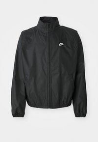 Sort Nike zip-up vindjakke med høj krave, elastiske manchetter, sidelommer og hvidt Nike-logo på brystet.