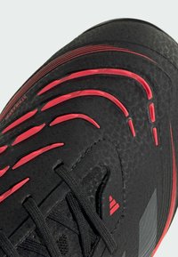 Black sneaker featuring textured upper with red accents and ridged design. Contains black laces and logo details on sides.