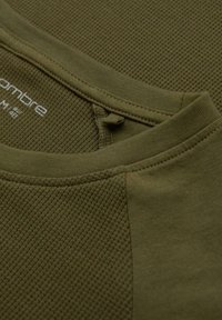 Camiseta verde oliva con un patrón de textura acanalada y un panel de tela suave. Escote redondo y detalles de costura visibles en toda la prenda.