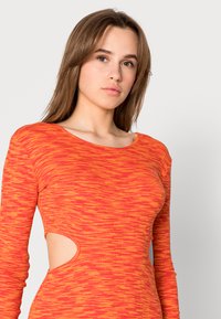Vestido de manga longa em gradiente de vermelho e laranja, com decote redondo e recortes na cintura. Textura suave e formato justo.