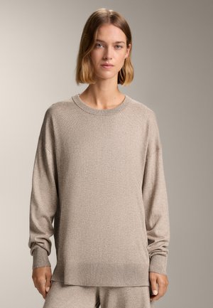 Beige gebreide trui met lange mouwen, geribbelde manchetten en zoom. Zachte textuur met een relaxte pasvorm, voorzien van een ronde hals en subtiele glans.